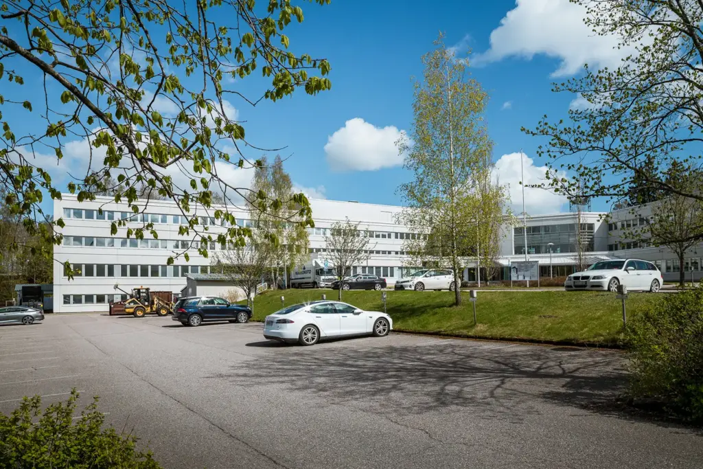 Valkea, neljäkerroksinen toimitilakiinteistö. L-mallisen rakennuksen edessä on autoja pysäköintialueella.