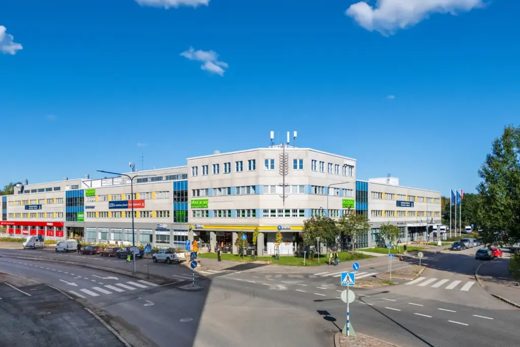 Helsingin Konalantie 47 julkisivu tien risteyksessä. Seinustalla yritysten logoja, mm. Puuilo, R-Kioski ja Liikku kuntokeskus.