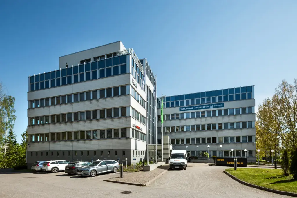 Vaalean toimitilakiinteistön julkisivu. Rakennuksen viereen on pysäköity muutamia autoja.