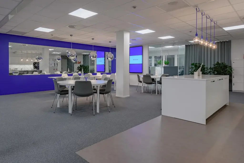 PRESSI Smart Premises B-talo avara taukotila. Tilassa on sininen tehosteseinä ja pyöreitä pöytiä.