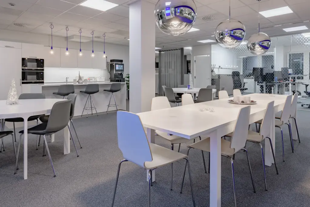 PRESSI Smart Premises B-talon tauko-/keittiötila. Istumapaikkoja on pöytien ja saarekkeen ääressä, keittiötiskillä on kahvikone. Katosta roikkuu peilipallovalaisimia.