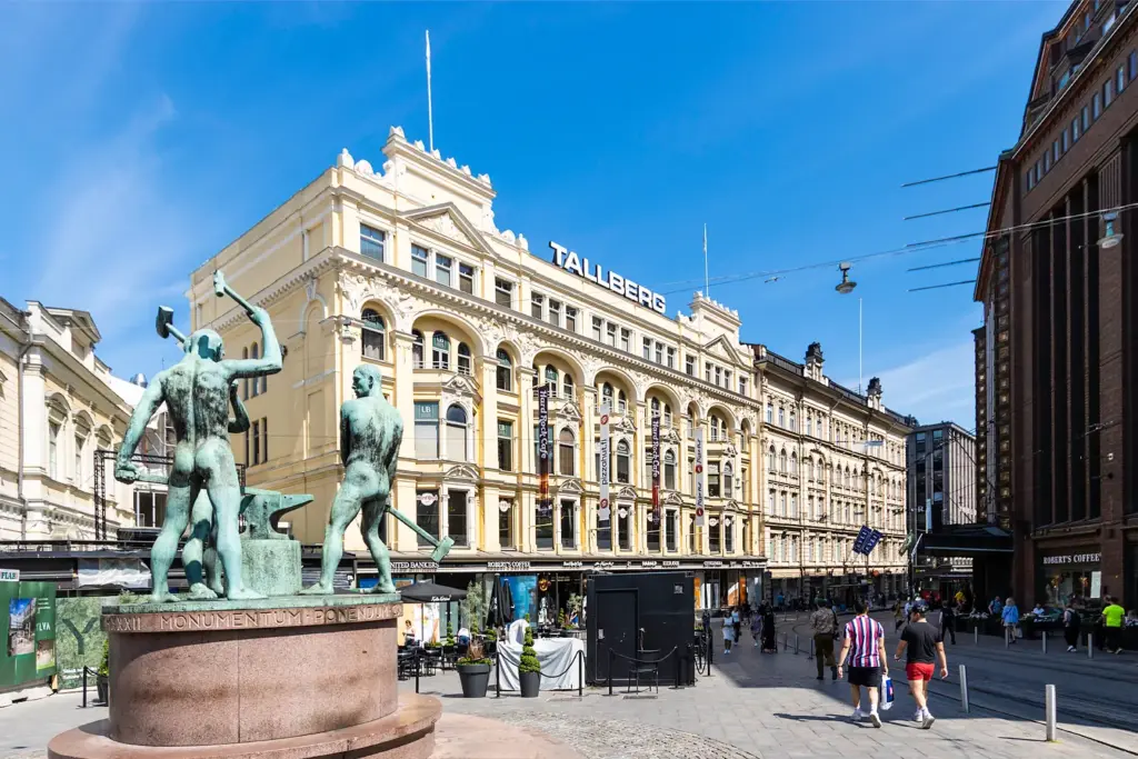 Aleksanterinkatu 21:n julkisivu. Rakennuksen edessä on kolmen sepän patsas ja Stockmannin tavaratalo.