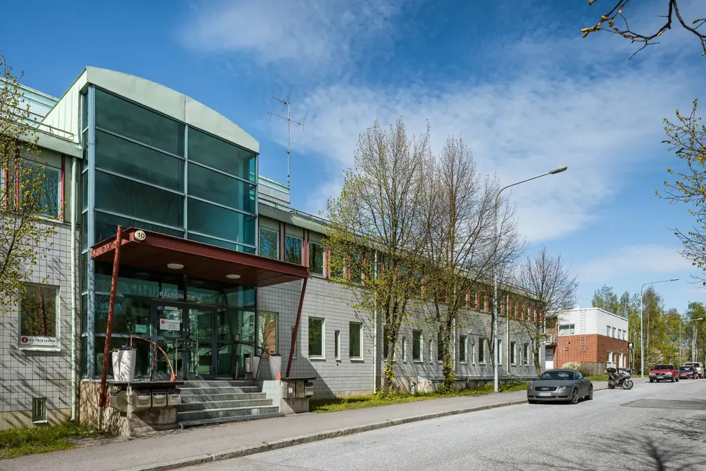 Helsingin Rälssintie 10-toimitilakiinteistön sisäänkäynti, jossa useamman metrin korkeat ikkunat ja punainen katos.