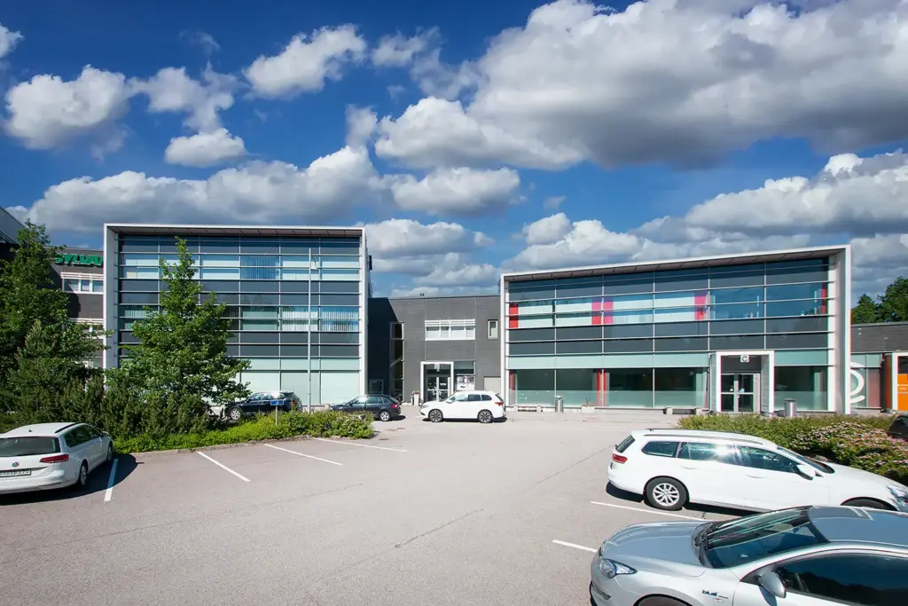 Kehämylly Business Parkin C- ja E-rakennukset. Talojen edessä on pysäköityjä autoja. Taustalla poutapilviä sinisellä taivaalla.